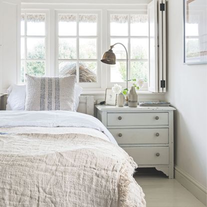 Neutral white painted bedroom with white and cream bedding and a chest of drawers next to it