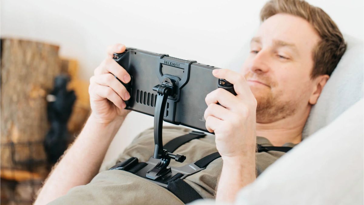 A man wearing a GoPro harness lies on a sofa or bed, playing a Steam Deck. The handheld gaming PC is mounted to the GoPro harness via grip and mount products from Mechanism.