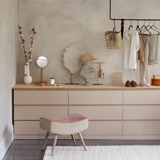 Pink dressing table with stool below clothing rail next to white rug