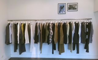 Clothes hang on a rail within a white room