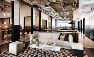 A white couch with coffee table and tables and chairs with oversized chandeliers with delicate metal frames in spun and mirror polish steel finishes