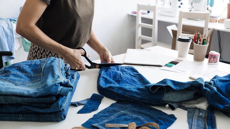 woman upcycling jeans on a table, to illustrate upcycled meaning