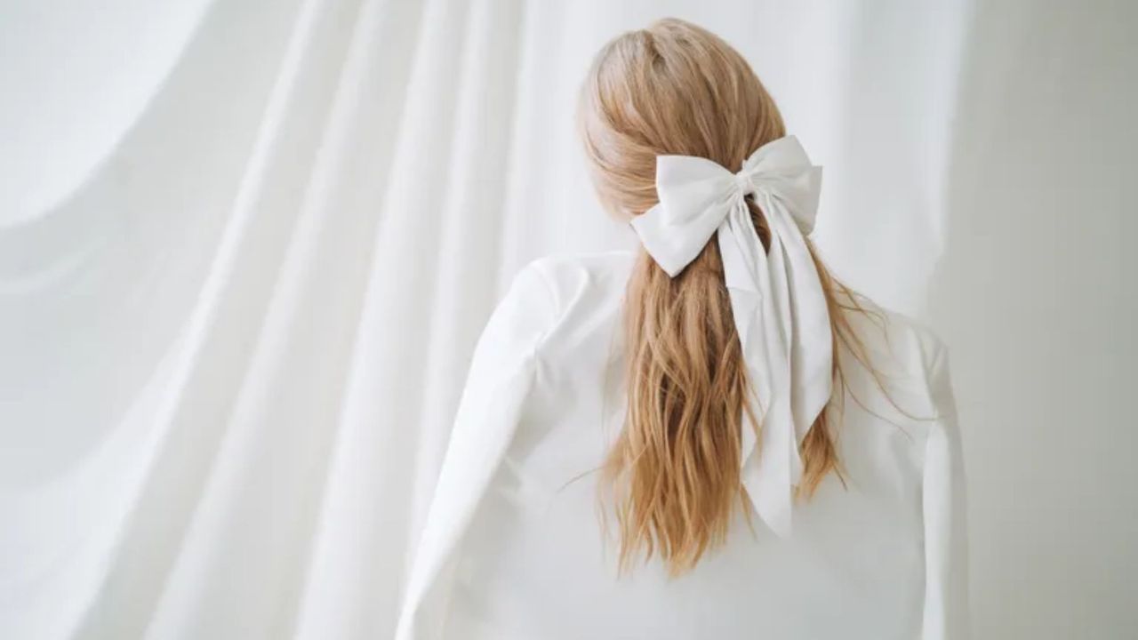 woman with blonde hair facing away from the camera with a white bow