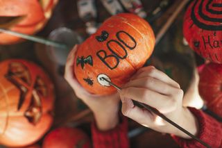 A person painting the word boo onto a pumpkin for Halloween.