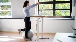 A woman standing at an electric desk stretching her arms