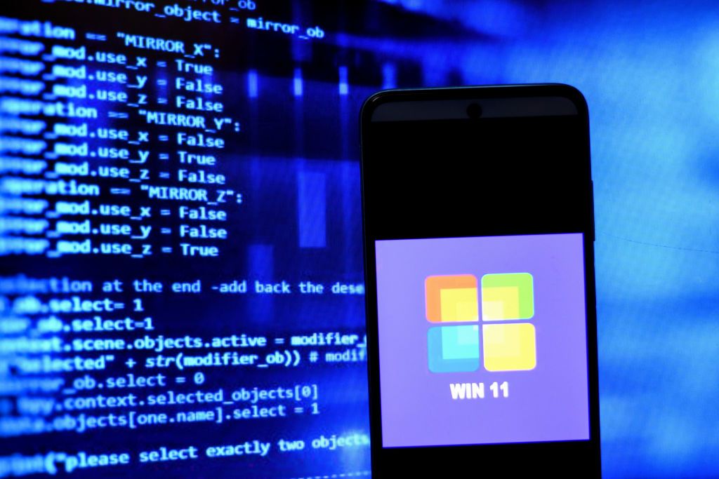 Win 11 on a smartphone in front of code on a monitor