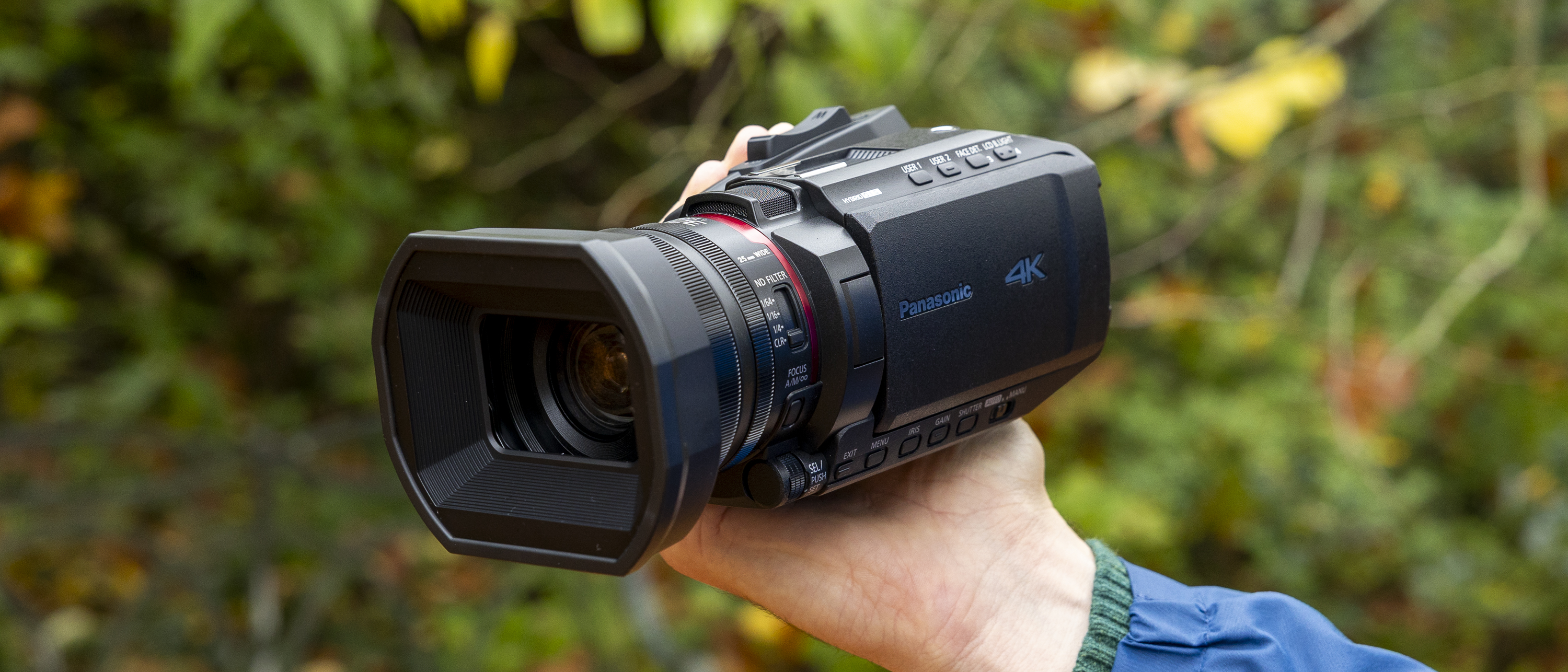 The Panasonic HC-X1200 camcorder held by a female photographer against an orange autumnal backdrop