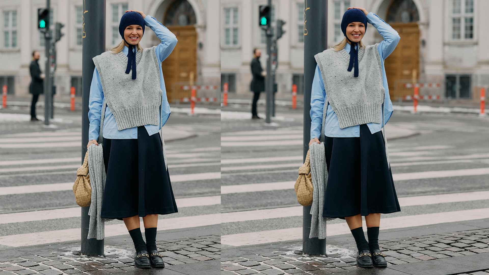 Woman poses while leaning on street lamp in front of a cross walk. She wears black skirt, button down shirt, gray sweater vest, and knitted babushka hat. 