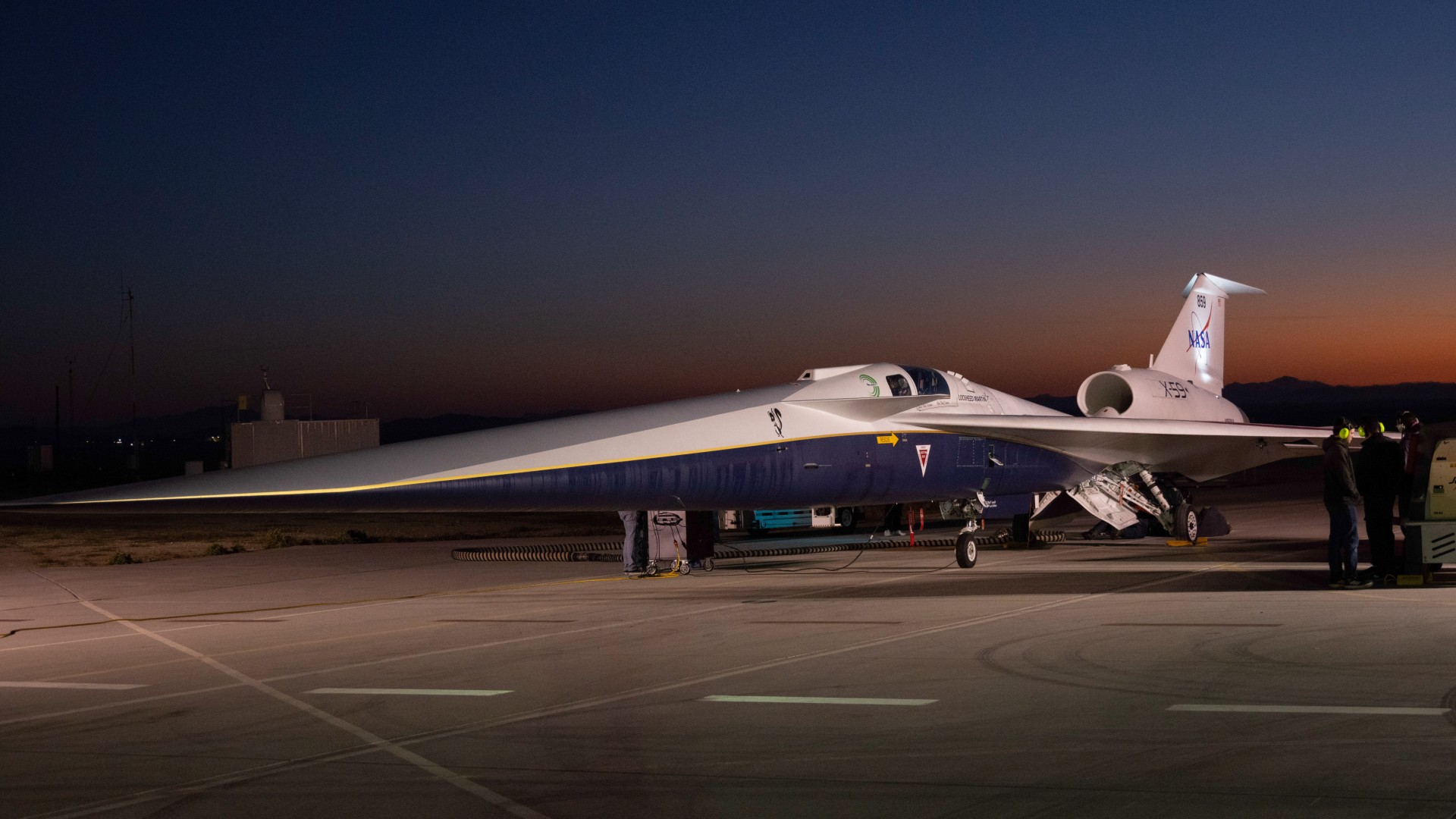 an elongated jet emblazoned with nasa logos sits on a tarmac at sunrise with the silhouettes of mountains visible in the distance