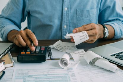 Man sitting at desk using a calculator and holding receipts