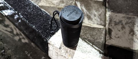 Tronsmart T7 portable Bluetooth speaker wet in the rain standing upright on a pavement outdoors