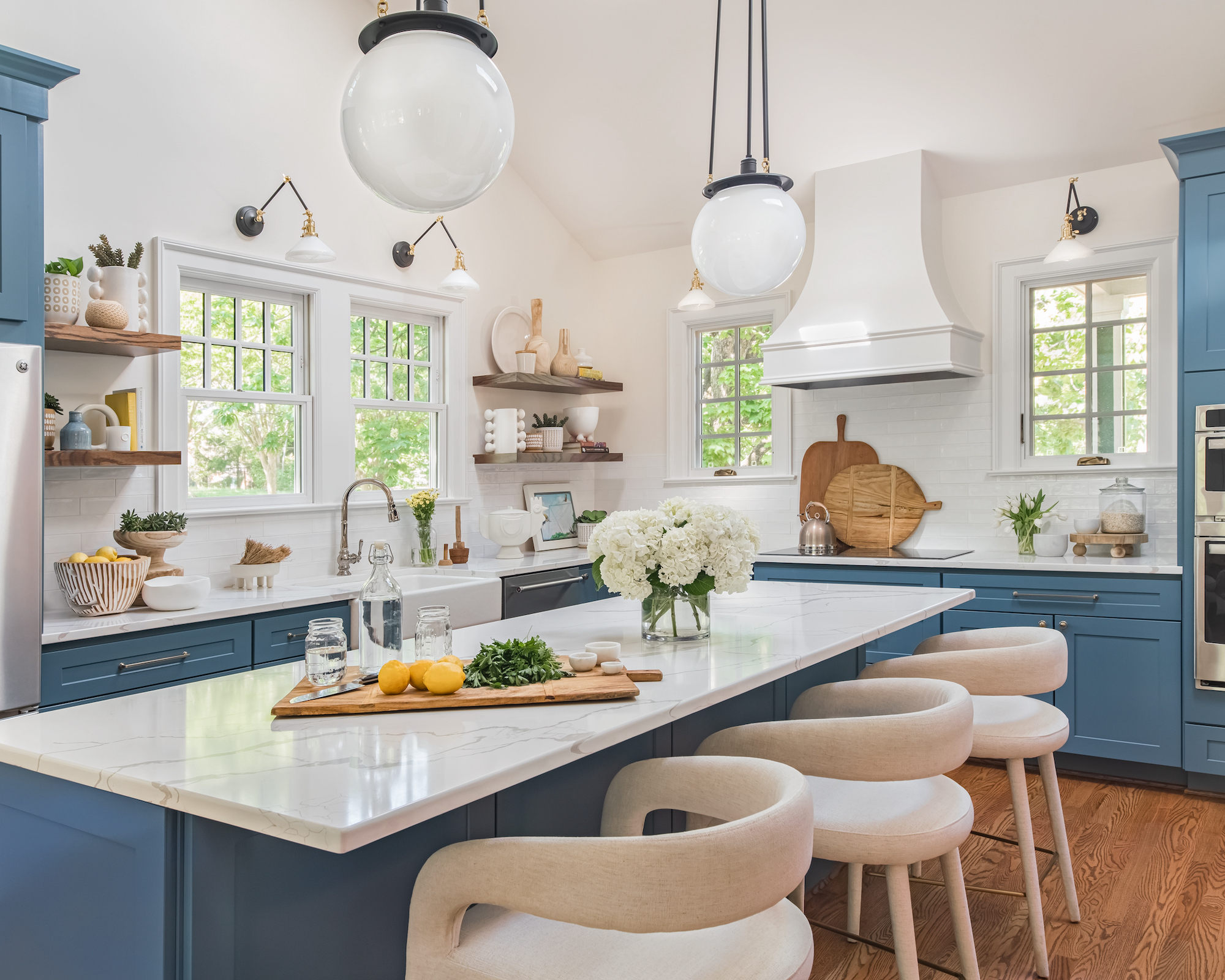 Kitchen with blue cabinets, light countertops, island with pendant lights over, upholstered stools and wood floor