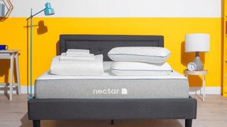 The Nectar Memory Foam mattress is placed on a dark grey bed frame in front of a bright yellow wall