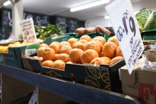 A photo of a market stall with a box or oranges in the foreground. Taken on a Fujifilm X100VI.