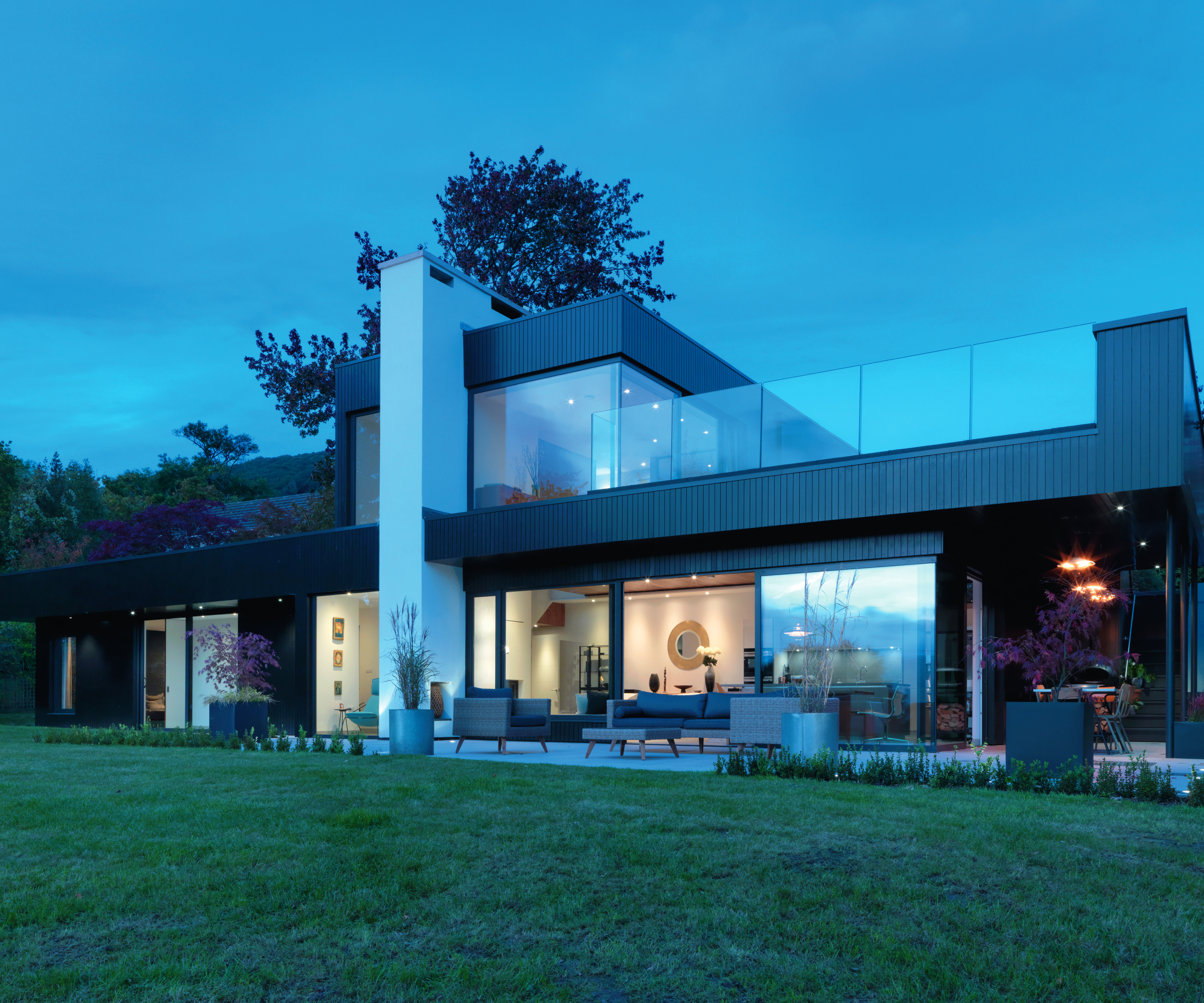 2 storey contemporary home shot at night with large glass balustrade around first floor terrace, large glazed windows and doors on lower ground floor