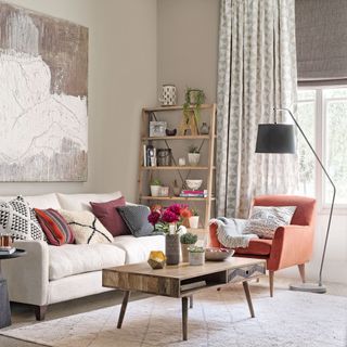 Neutral living room with coffee table, cream sofa, orange armchair and window with curtains and blinds