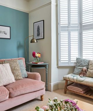 view towards bay window in living room with pink sofa, blue and white walls and window shutters