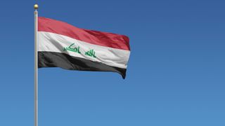The flag of Iraq flying against a pale blue sky
