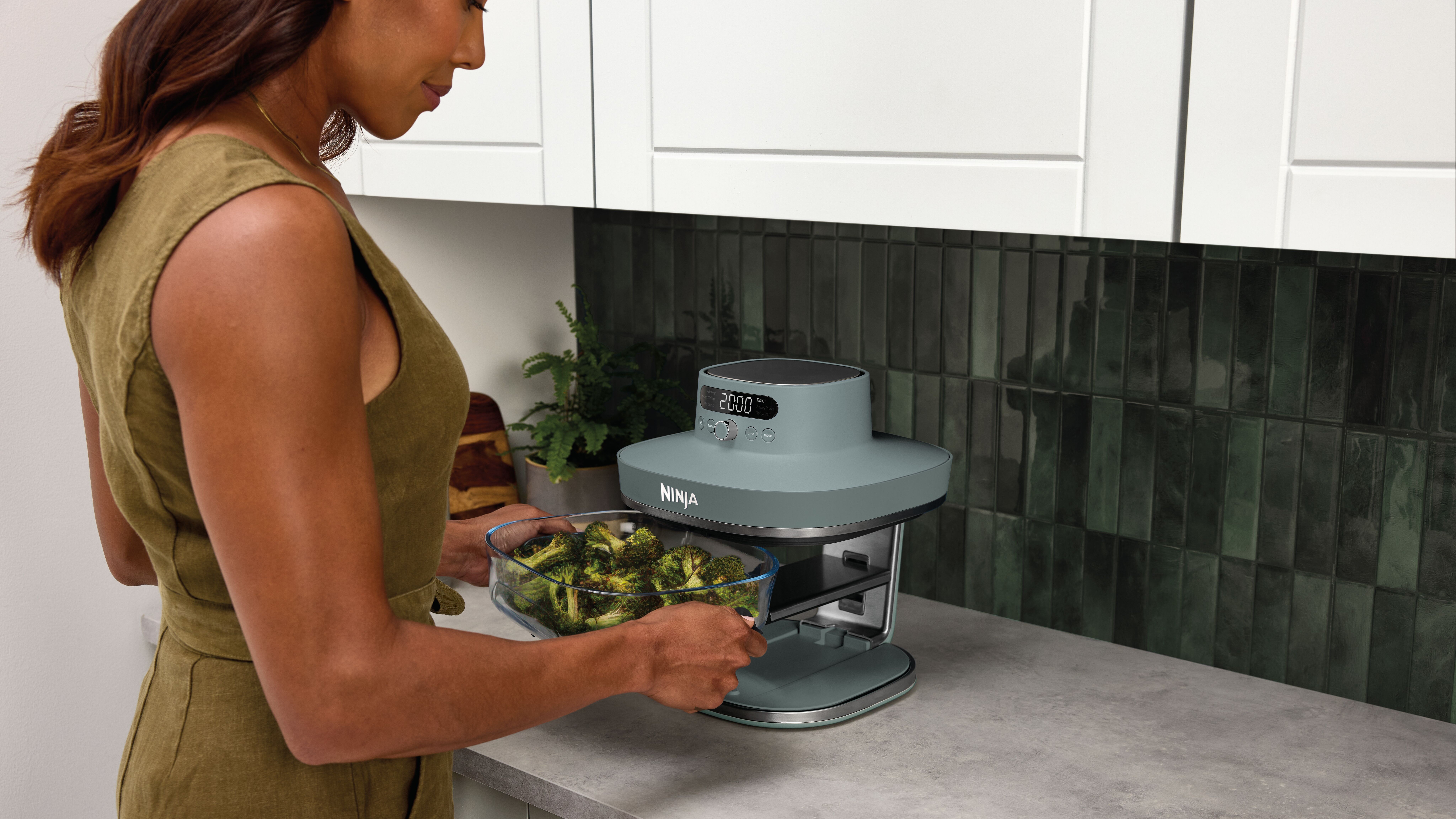 Woman putting dish of broccoli into Ninja Crispi Pro air fryer