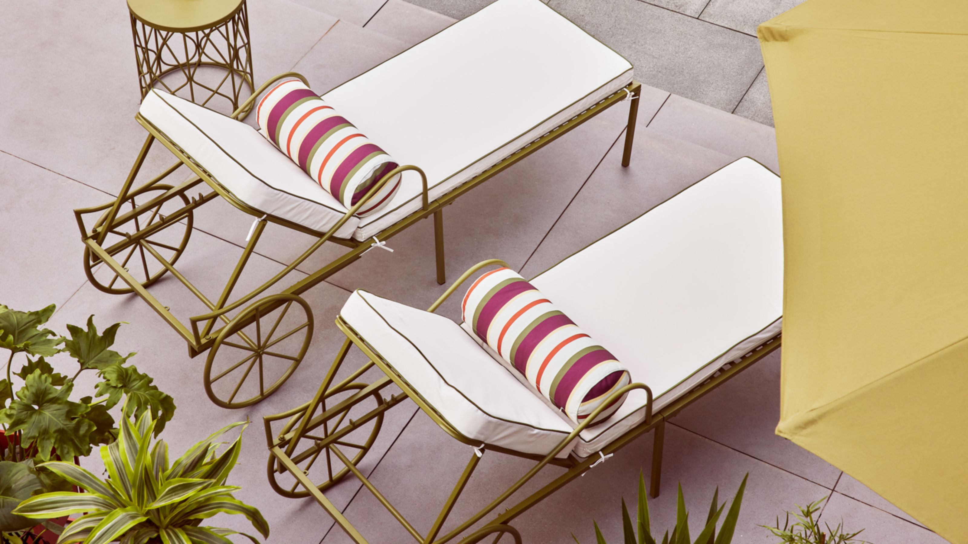 sun loungers from QVC studio 70 collection by a pool with green side table with green parasols, and green plants