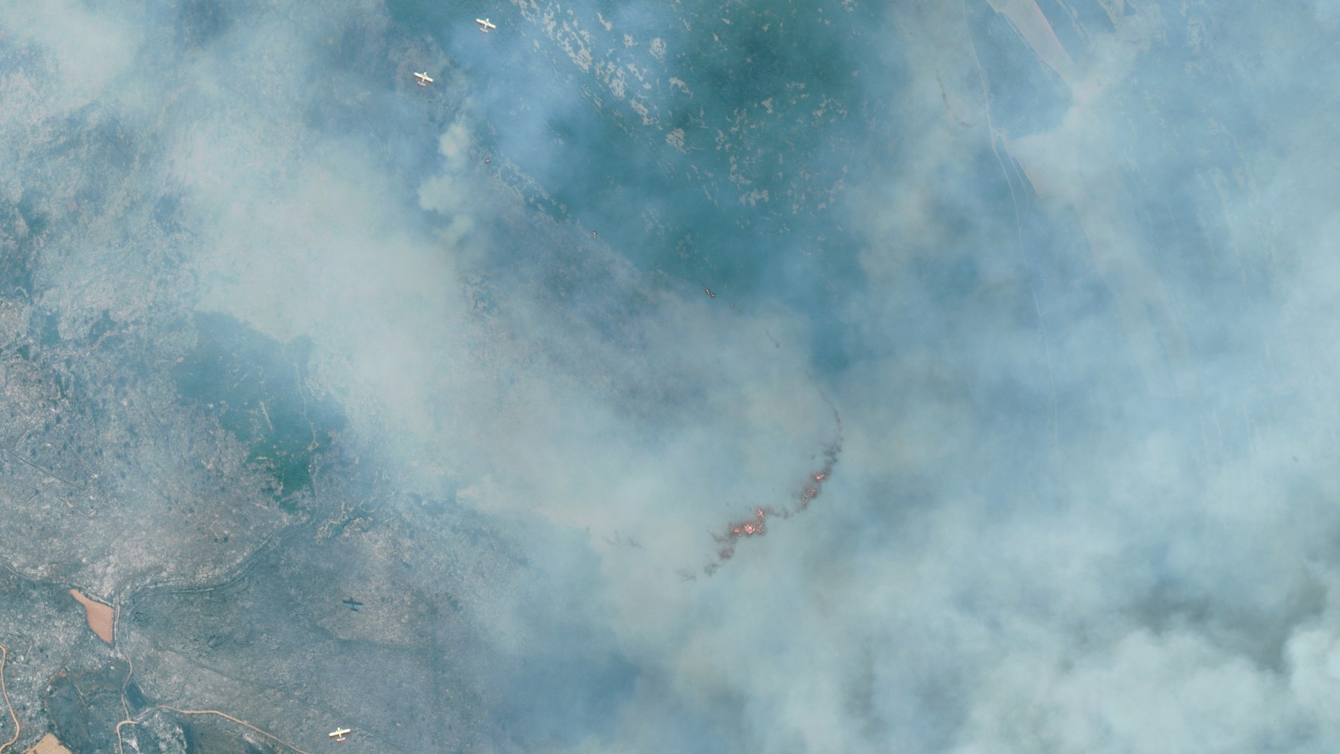 fire and smoke rolls through a green countryside as seen from space