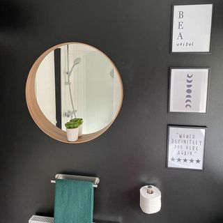 Dark walled bathroom with hanging mirror and photo frames on the wall