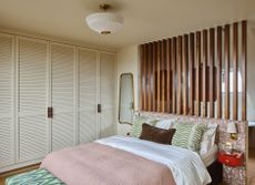 A bed with white wardrobes, and a slatted design between the bedroom and bathroom
