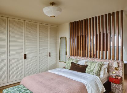 A bed with white wardrobes, and a slatted design between the bedroom and bathroom
