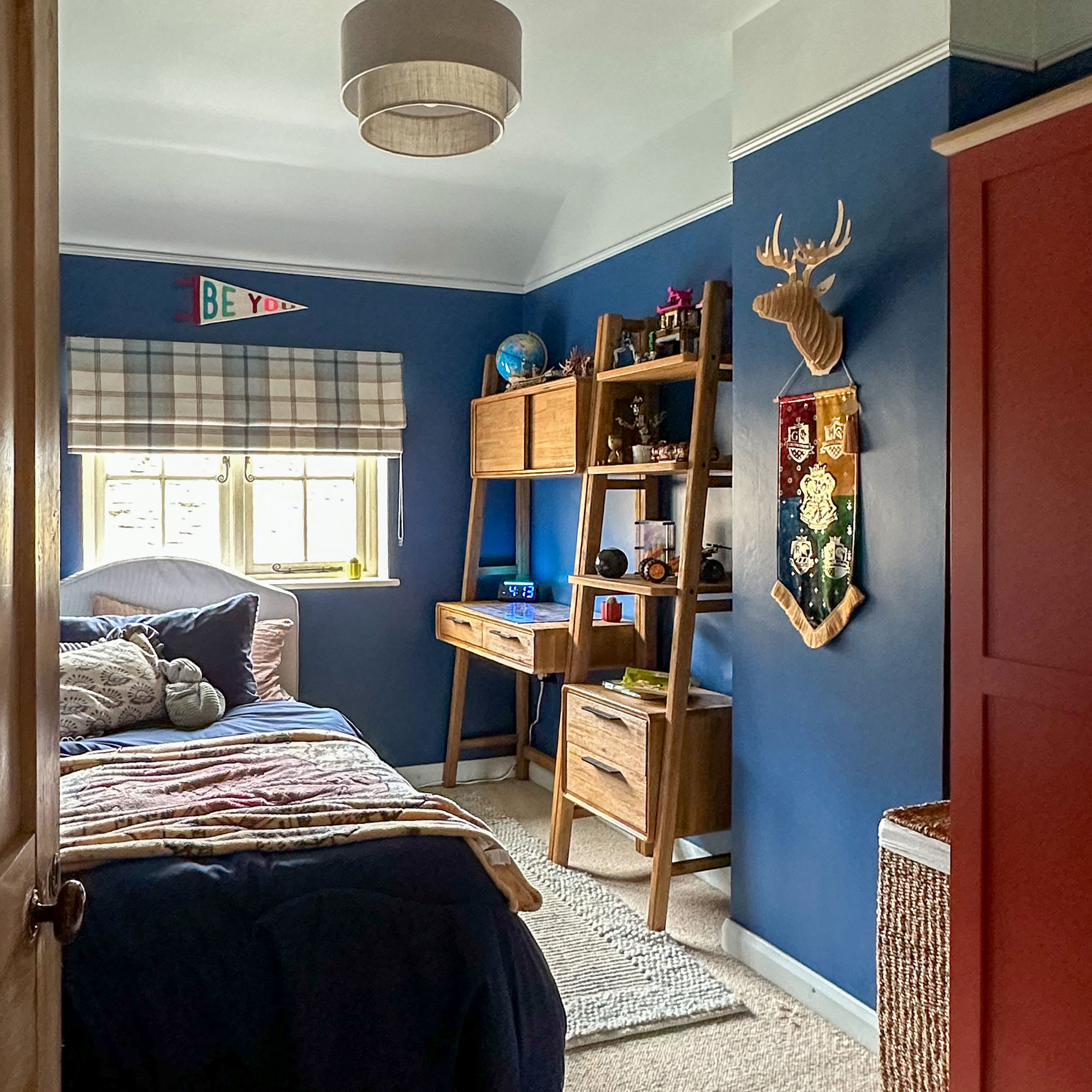 Blue boy's bedroom with twin bed, tartan window blind and wooden furniture
