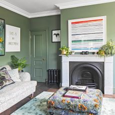 a green painted colour drenched living room with patterned sofa and footstool and a fireplace with plenty of striking artwork on the walls