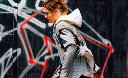 A person seen side on walking past a black wall covered in graffiti. 