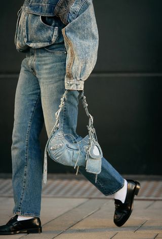 a close up photo of a woman wearing a double-denim outfit with loafers and a second-hand balenciaga bag