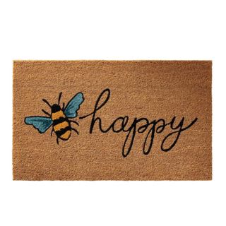 A toasty brown doormat with a black and yellow bee illustration with cursive black writing that says 'happy'