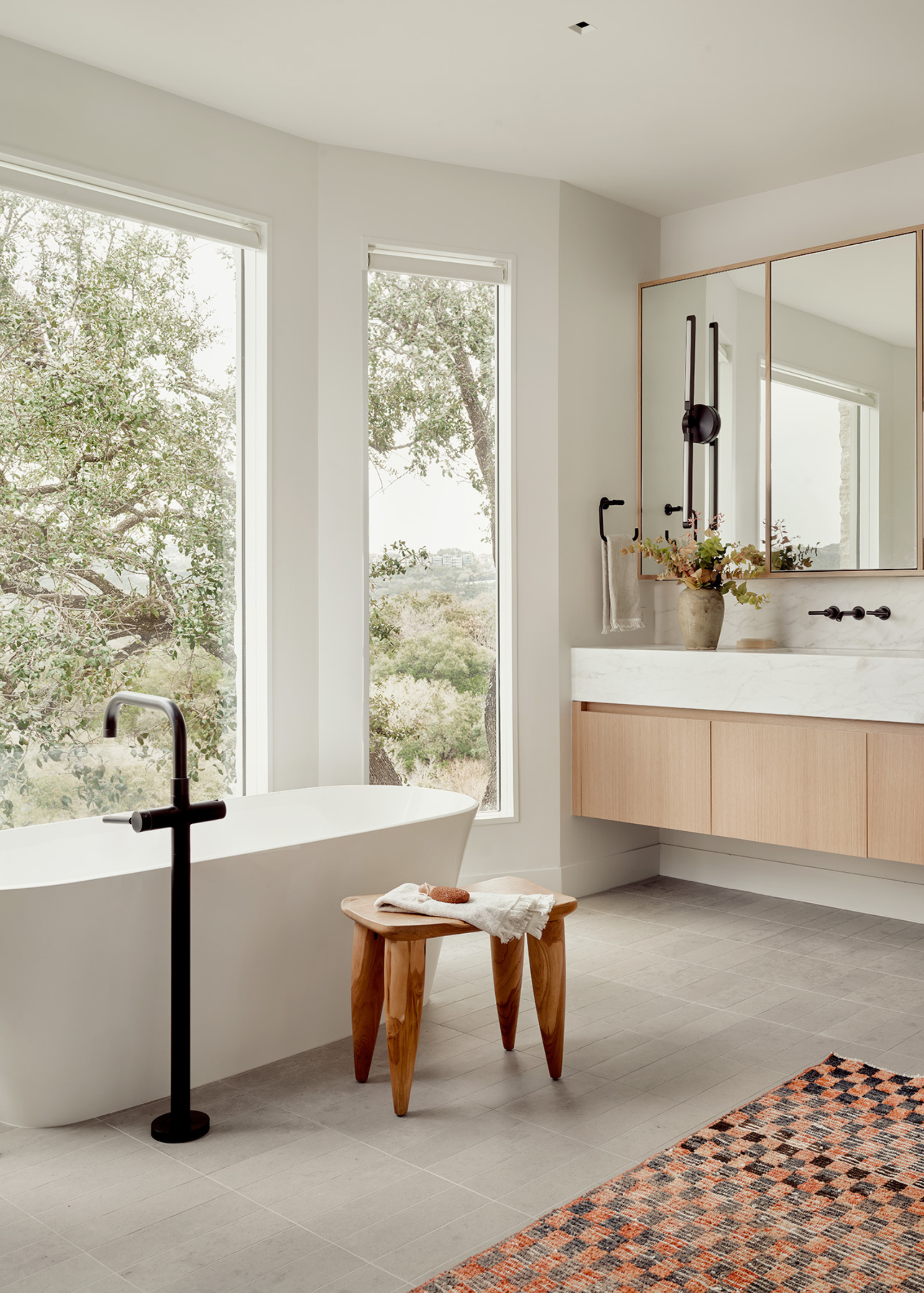A white bathroom with a checkerboard rug, large windows, a standing tub, a bath stool and a towel