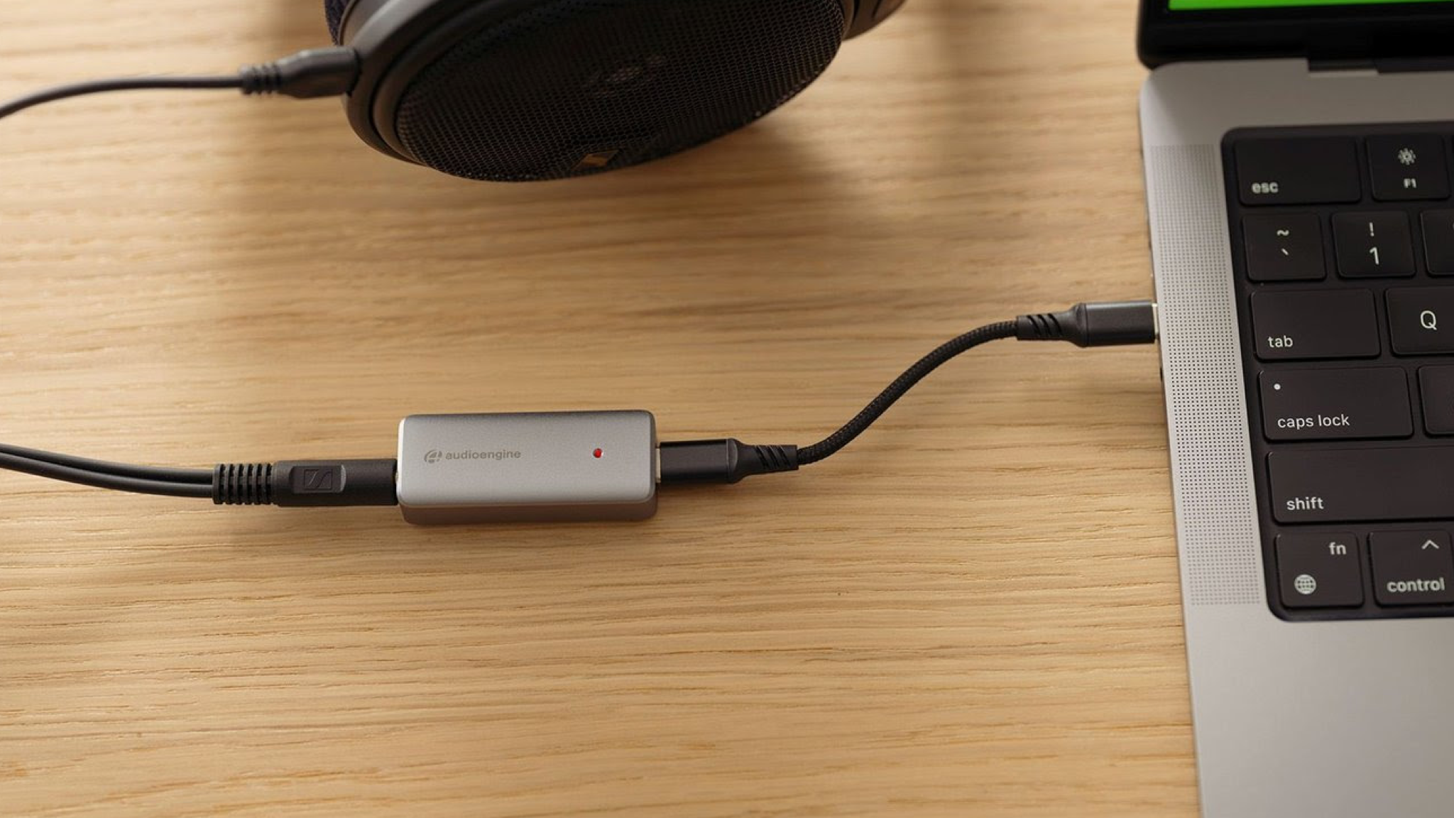 Audioengine HXL headphone amp and DAC on a desk connected between headphones and an Apple laptop