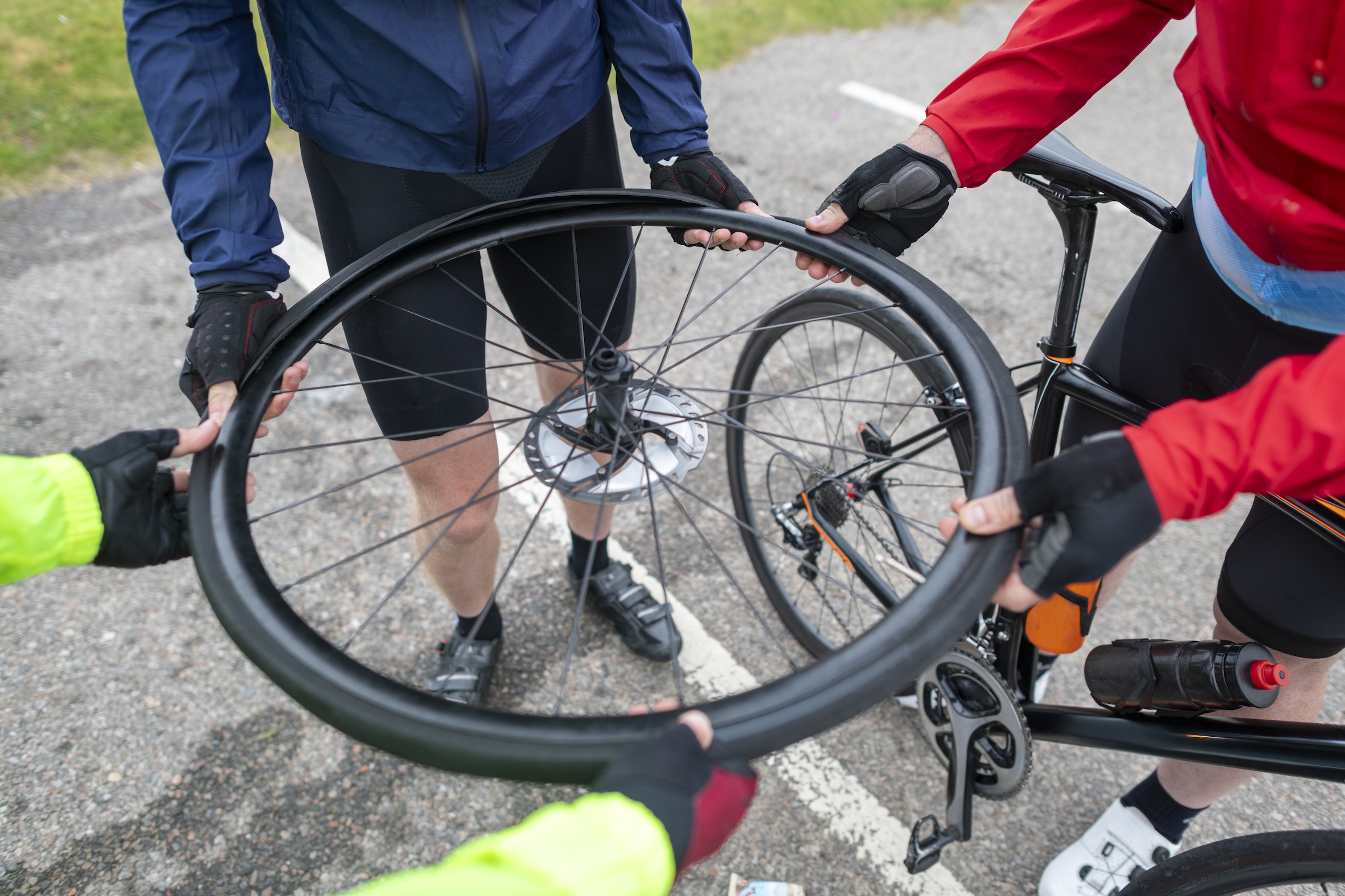 four cyclists holding a bicycle wheel with the tyre half off