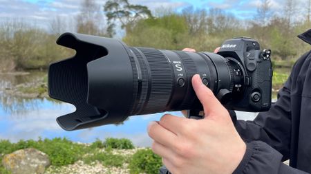 Mike Harris holding Nikon Z 70-200mm f/2.8 VR S II by a lake with vegetation and trees in the background 