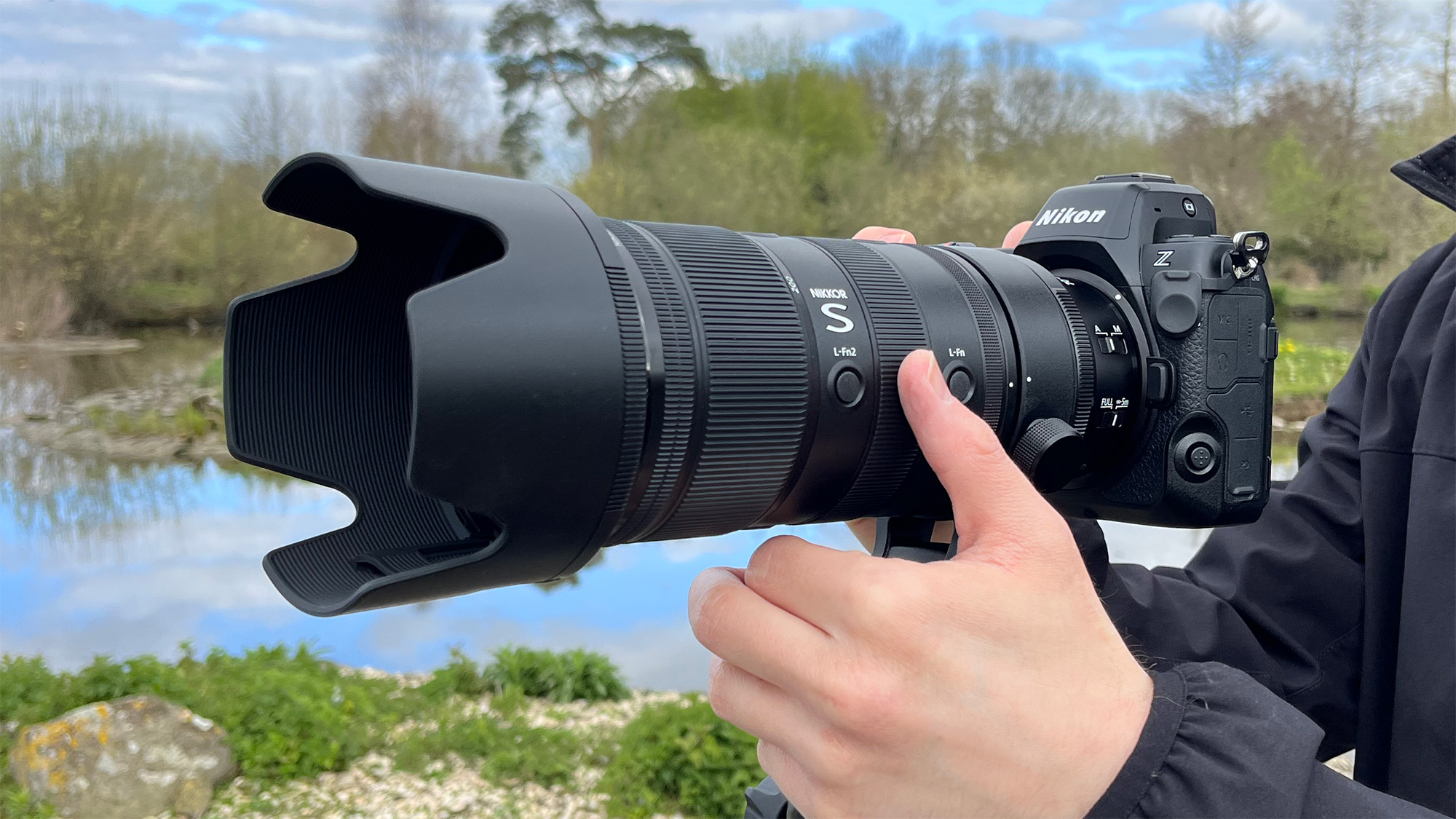 Mike Harris holding Nikon Z 70-200mm f/2.8 VR S II by a lake with vegetation and trees in the background