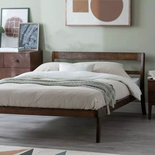 A dark wood bedframe in a green bedroom with a cream duvet on the top