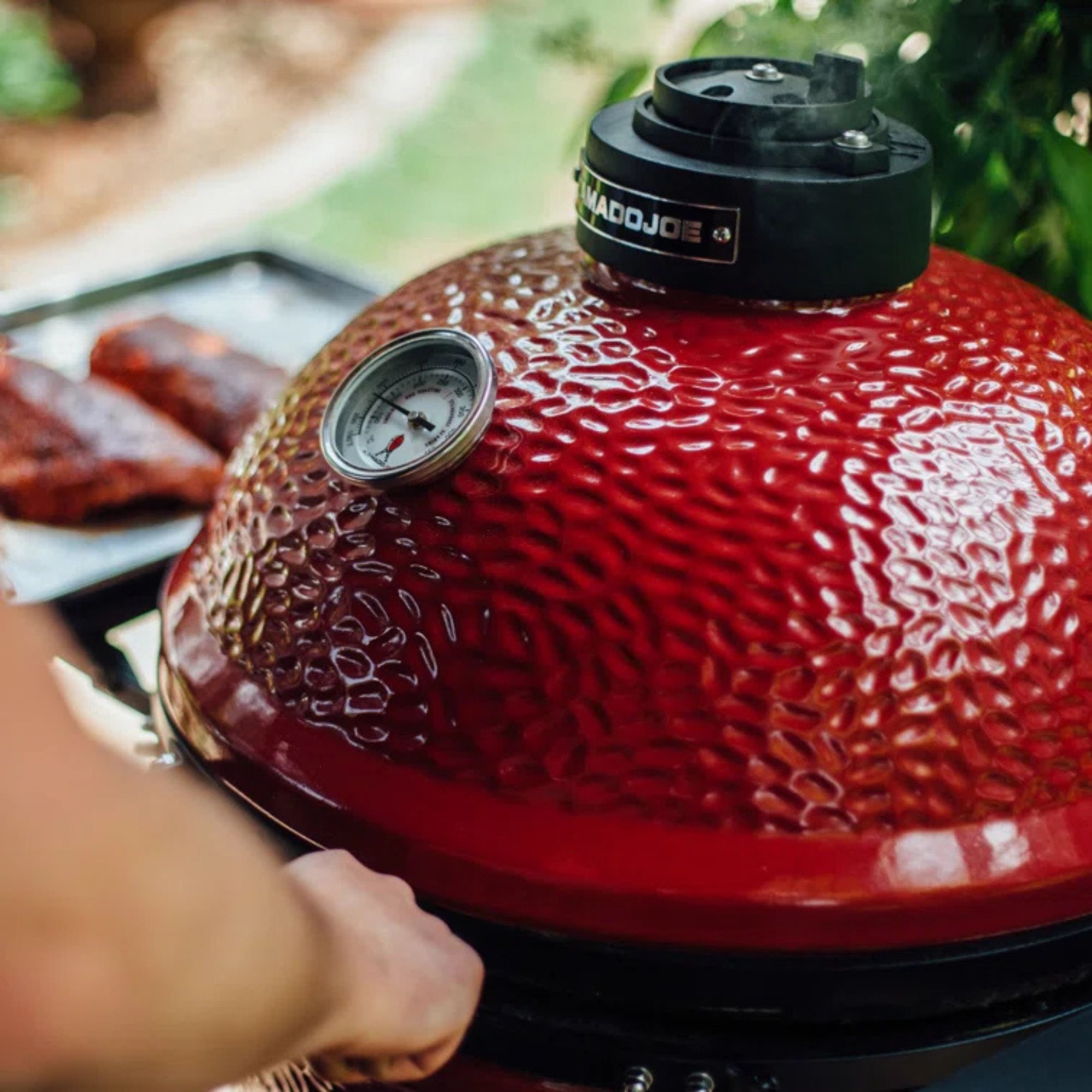 A hand opening the Kamado Joe ClassicJoe.
