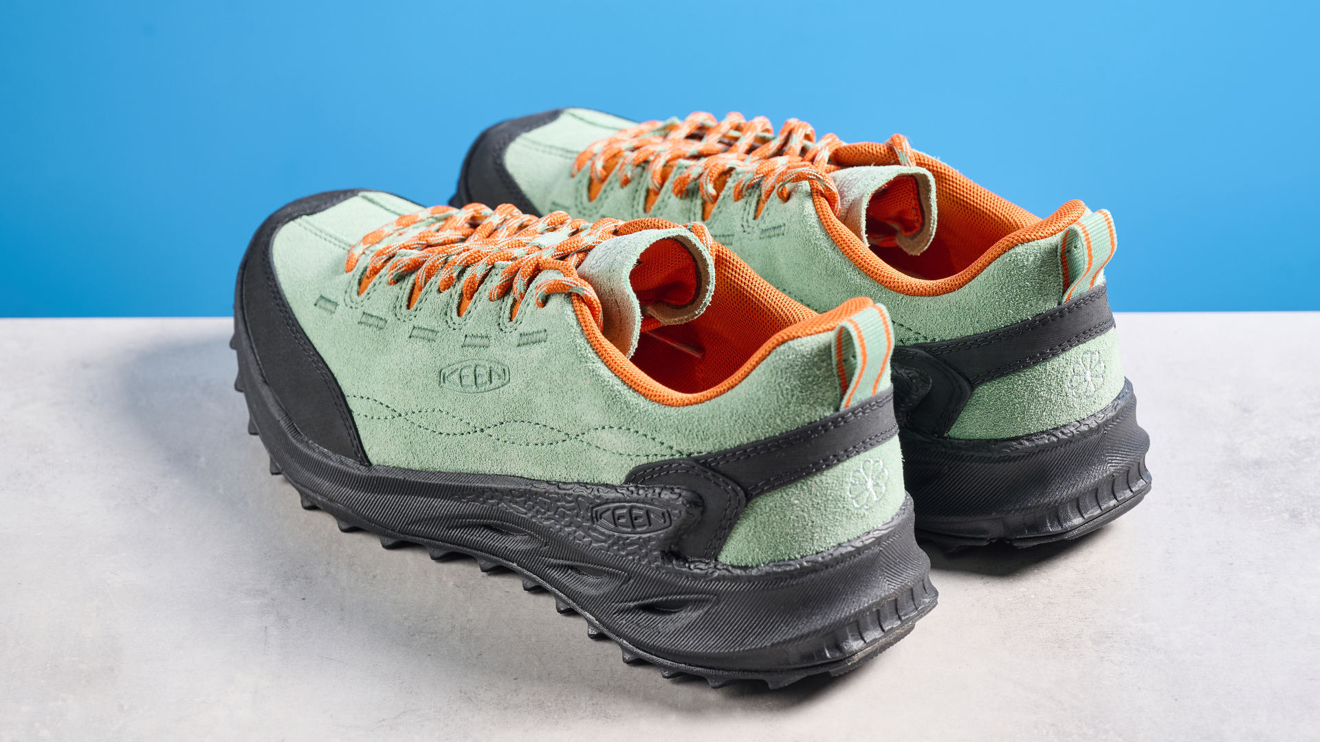 The Keen Jasper zionic hiking shoes in green/gold colorway are photographed against a blue Tom&#039;s Guide background and a stone floor, showing the lug sole and the leather upper with orange laces