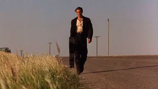 The Mariachi walks down a desert road carrying a guitar case in Desperado