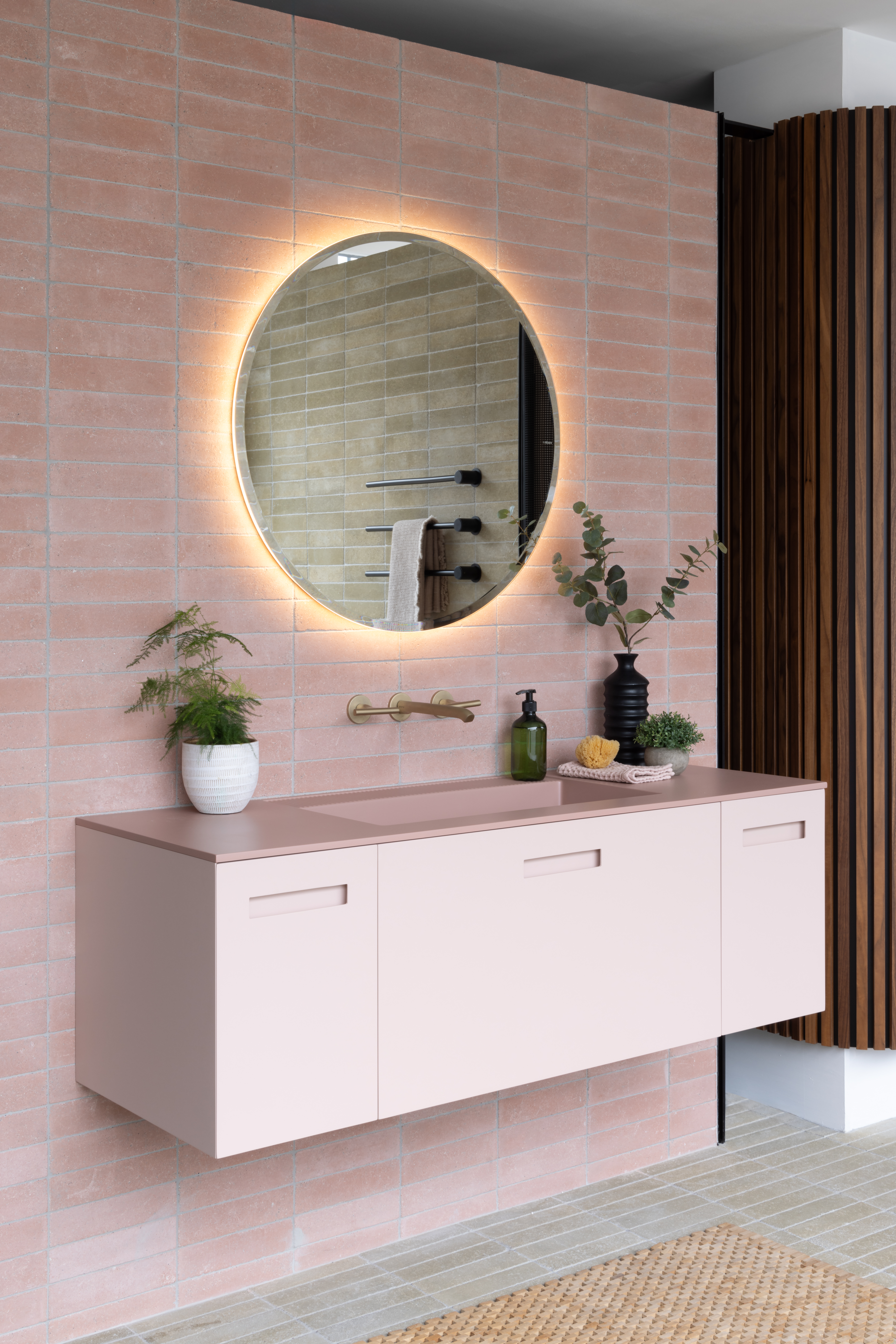 Full baby pink bathroom with tiled wall, pink vanity with a built in sink, and a back lit round mirror