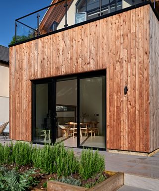 A timber clad exterior with bifold doors opening out onto a patio of a self build home