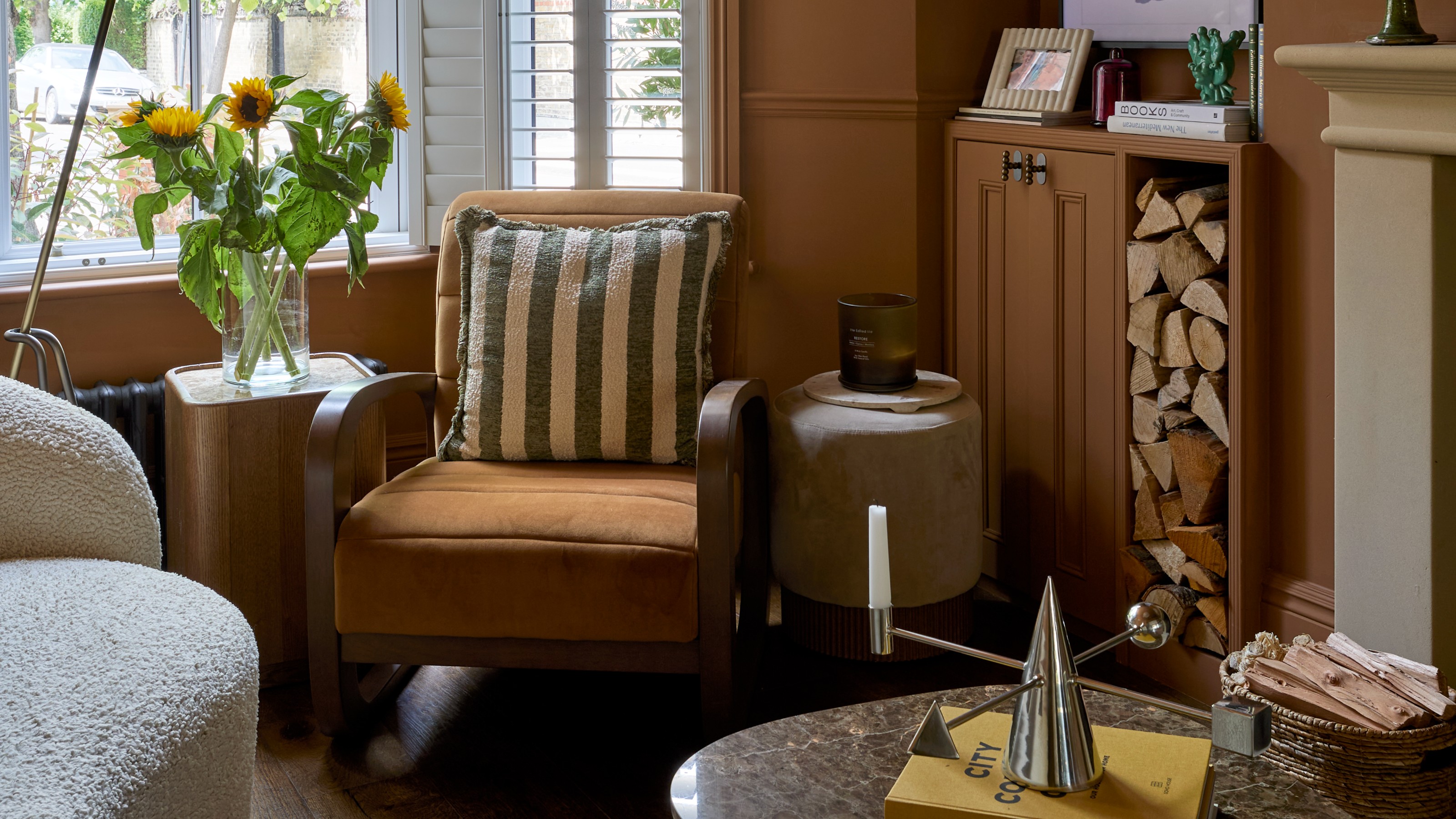 A narrow living room painted in a warm brown shade with and a curved white boucle sofa with a dark marble curved coffee table
