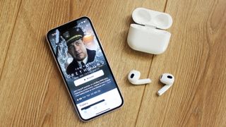 airpods 3 ligger på ett bord bredvid en iPhone och sitt tillhörande laddningsfodral.