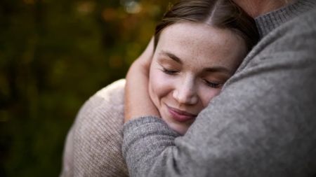 close up on a woman's smiling face as she leans into the chest of another person during a hug