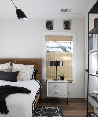 Contemporary bedroom with white and cream painted walls, dark wooden flooring with black rug, shelving unit, bed with white linen, scatter cushions