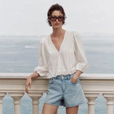 Woman wears white blouse, blue denim shorts, sunglasses