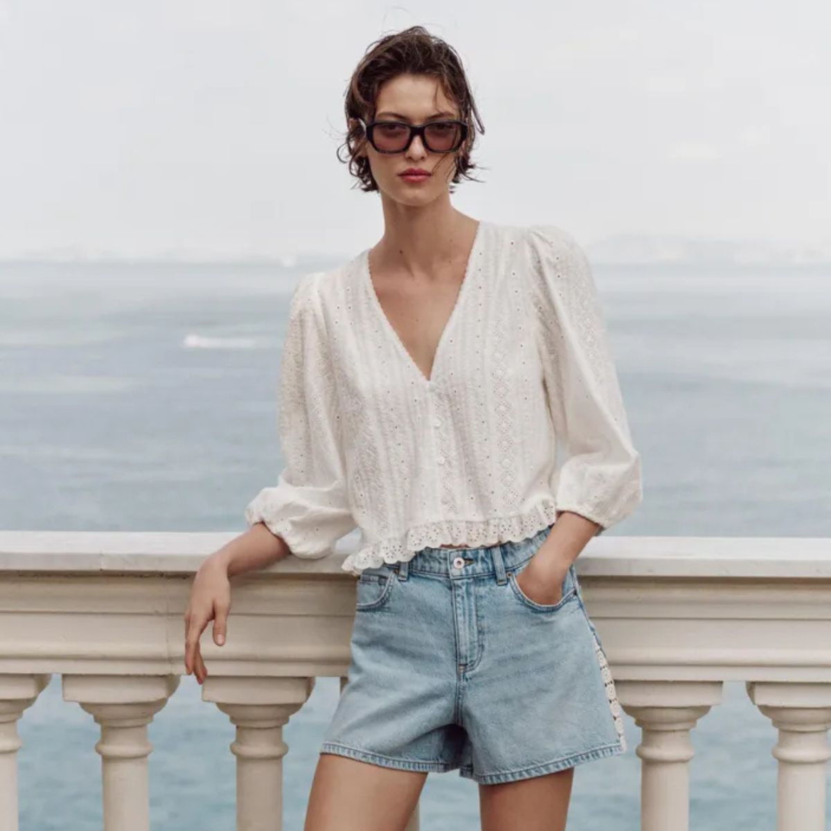 Woman wears white blouse, blue denim shorts, sunglasses